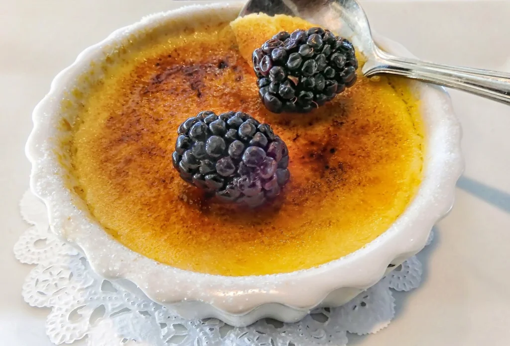 Crab brulee served in a ramekin topped with fresh blackberries for added elegance.